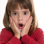 Surprised little girl with hands touching her face isolated on white background